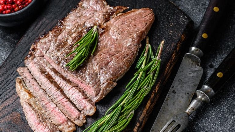 air fryer round steak sliced on a board and garnished with rosemary sprigs
