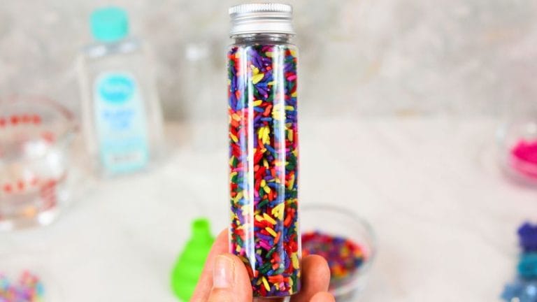 a hand holding an easy DIY mini sensory bottle full of rainbow rice