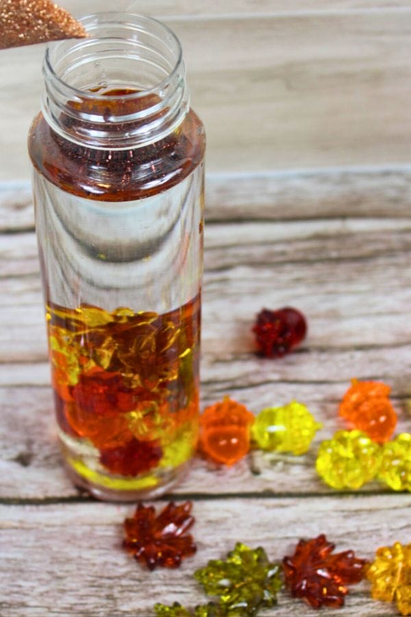 a sensory bottle being filled with fall colors of glitter and plastic leaves