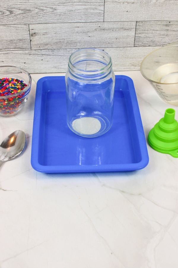 a jar on a blue tray with supplies for a science experiment for toddlers