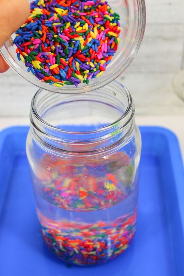 rainbow rice going into a magic dancing rice science experiment jar on a tray