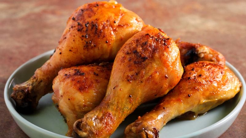 Four leftover roasted chicken drumsticks rest on a vibrant green plate, ready to be enjoyed.