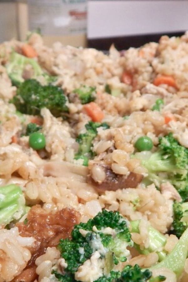 A close-up of fried rice featuring leftover chicken drumsticks, vibrant broccoli, peas, and carrots.