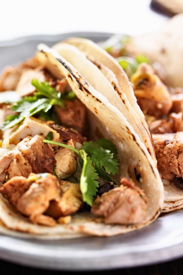 Close-up of tacos featuring leftover chicken drumstick meat, cilantro, and soft tortillas on a plate.
