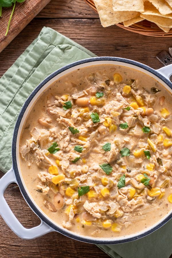 A pot of creamy chili crafted from leftover chicken drumsticks, enhanced with corn and white beans, and garnished with fresh cilantro.