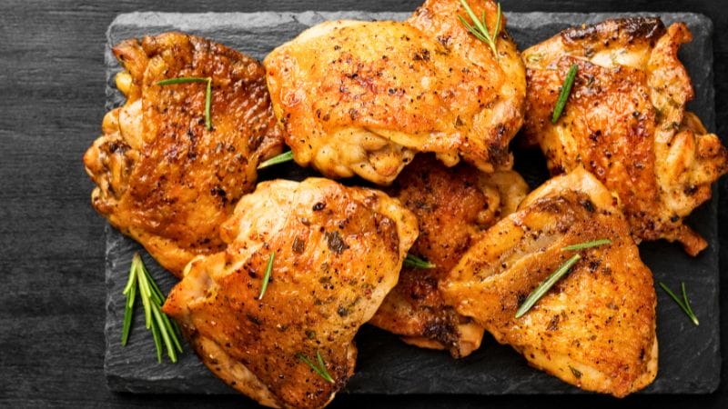 Leftover grilled chicken thighs with rosemary are elegantly displayed on a black slate serving board.