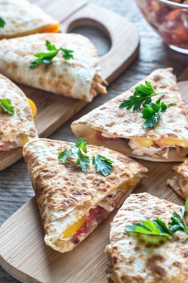 Close-up of sliced quesadillas on a wooden board, garnished with fresh parsley. Some are packed with flavorful leftover chicken thighs, tomatoes, and melted cheese.
