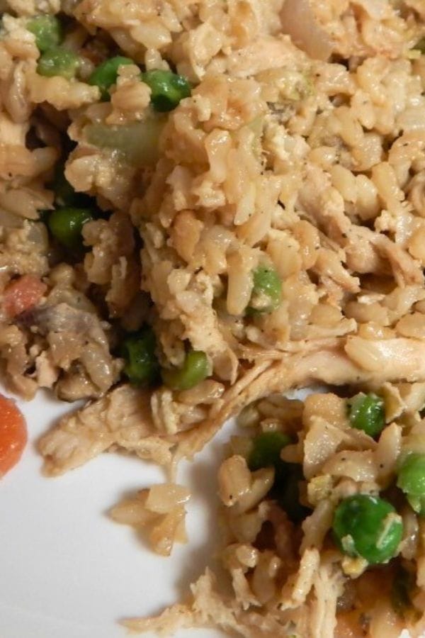 Close-up of a mixed rice dish with peas, carrots, and shredded chicken on a white plate, reminiscent of the comforting flavors found in a broccoli tuna casserole.