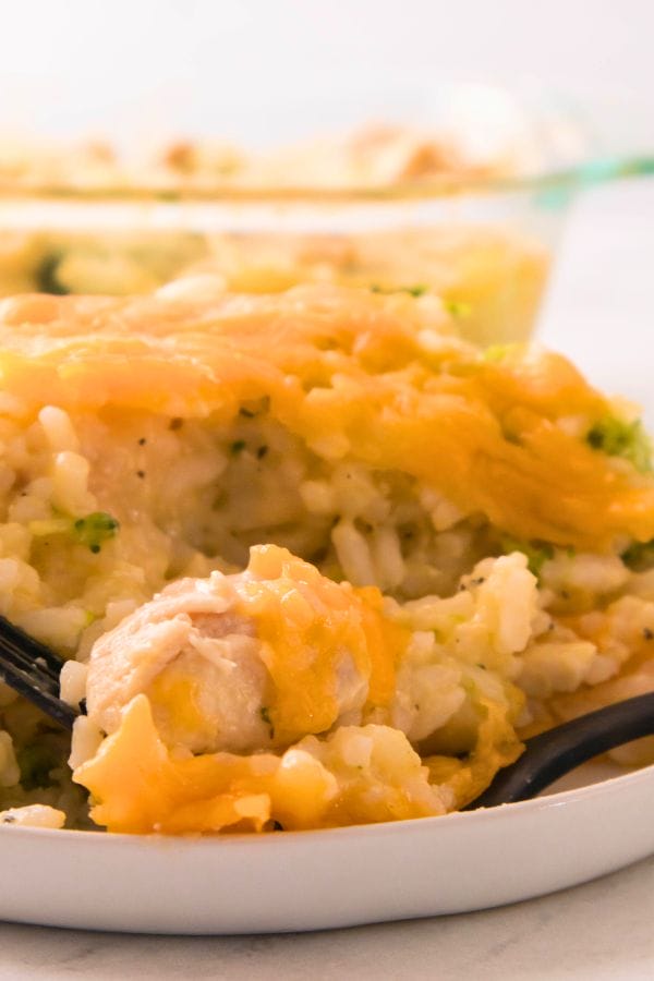 Close-up of a plate with a cheesy chicken and broccoli casserole, showcasing rice intertwined with melted cheese, and a fork teasingly poised at the edge.