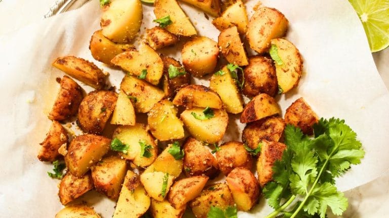Roasted potato wedges with seasoning and cilantro sit on a piece of parchment paper