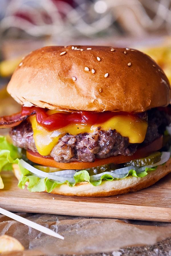 A hamburger with cheese, ketchup, bacon, lettuce, tomato, pickles, and onions on a sesame seed bun