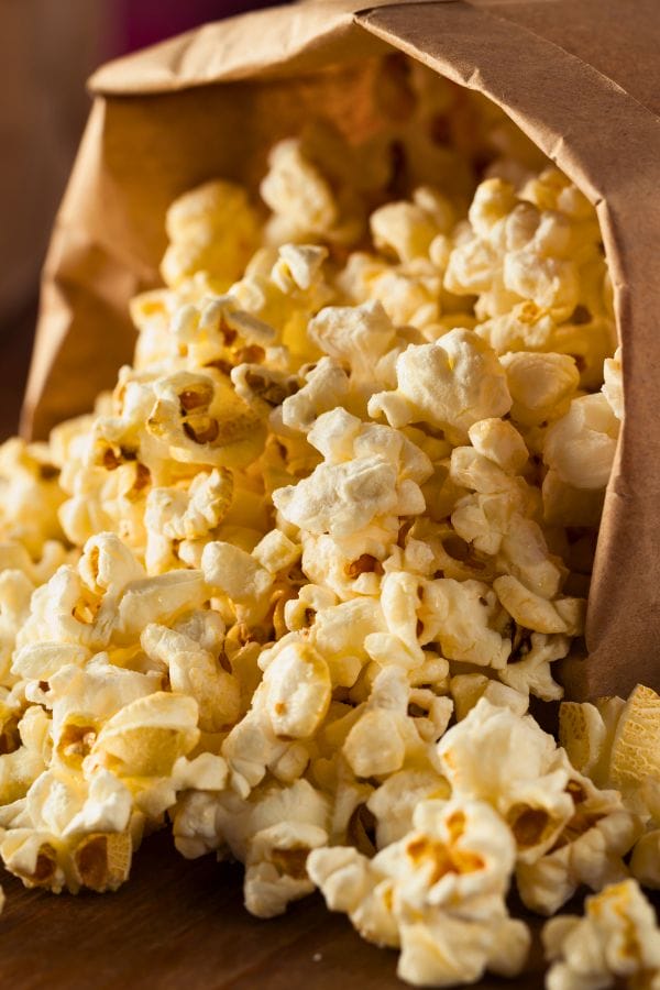Popped popcorn spilling out of a brown paper bag onto a wooden surface, 