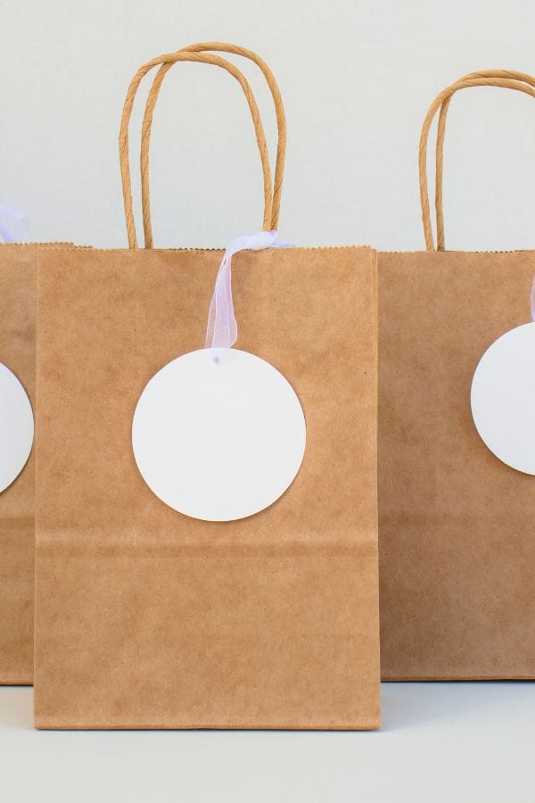 Three brown paper gift bags with twisted handles sit side by side, each featuring a round white tag attached by a ribbon, reminiscent of the warm camaraderie 