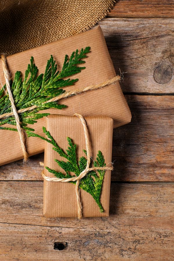 Two brown paper-wrapped gifts tied with twine and decorated with evergreen sprigs rest on a wooden surface