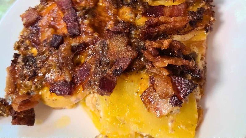 A plate featuring a slice of cheesy potato casserole reminiscent of a cheeseburger and fries, topped with crispy bacon pieces.