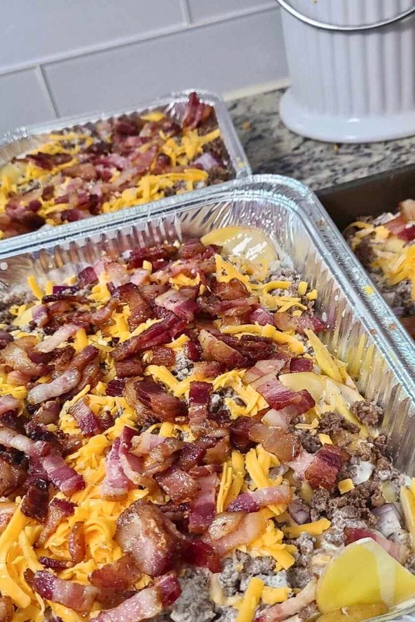 Close-up of two aluminum trays filled with a delectable Cheeseburger and Fries Casserole, layered with cheese, bacon, and ground meat.