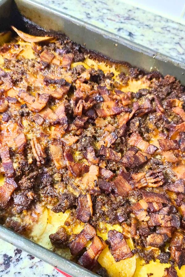 Casserole with browned, crispy bacon and ground meat topping on a golden crust, reminiscent of a classic cheeseburger and fries, in a rectangular metal baking dish.