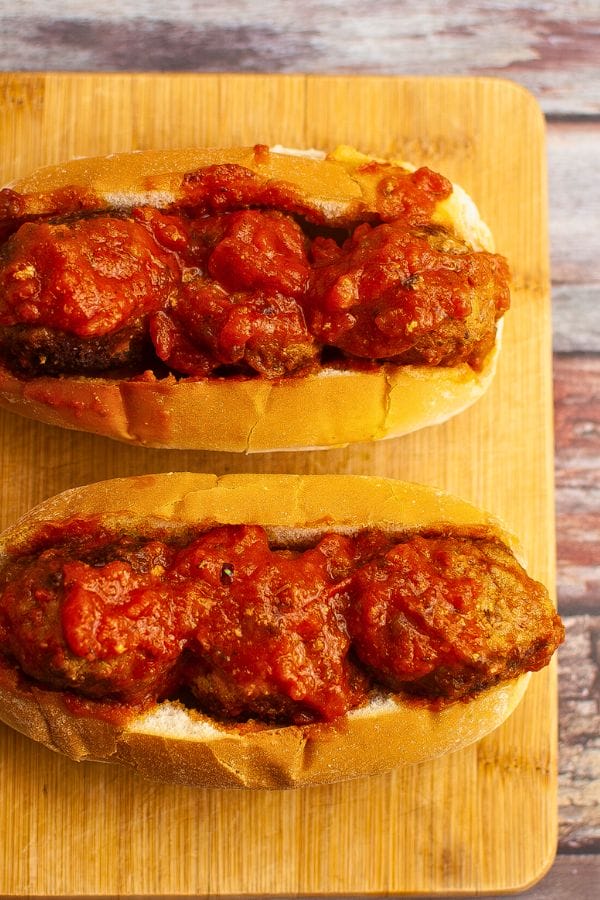 Two meatball subs with tomato sauce rest on a wooden board