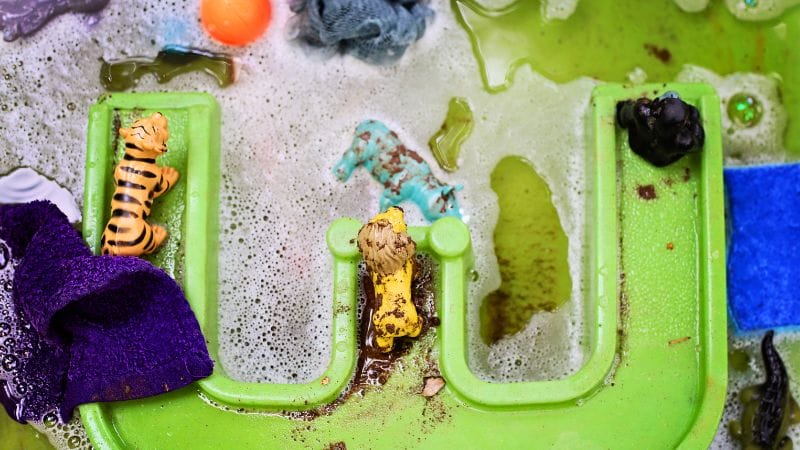 A zookeeper's delight, plastic animal toys and various objects splash around in soapy water, creating a fun animal care activity.