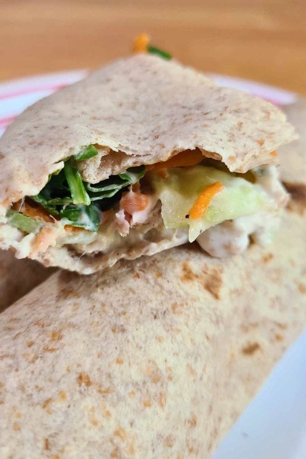 A close-up of a sliced healthy tuna wrap filled with vegetables and sauce, elegantly placed on a plate.