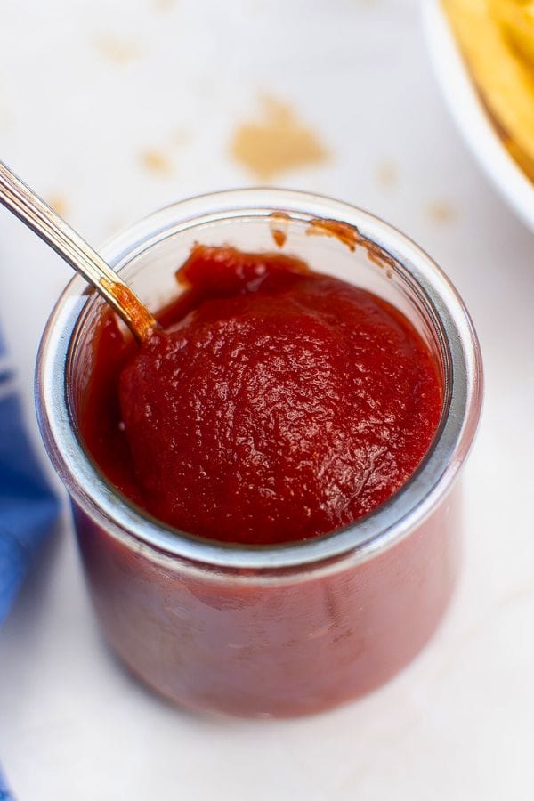 A jar filled with thick, red ketchup sits invitingly, its spoon poised