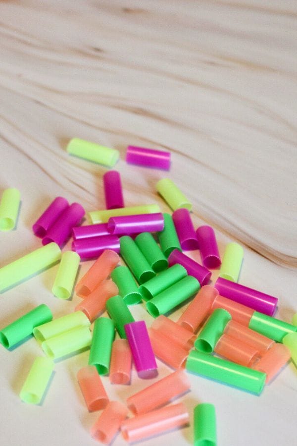 A sprinkle of colorful, short plastic tubes is scattered across the light wooden surface, resembling playful confetti.