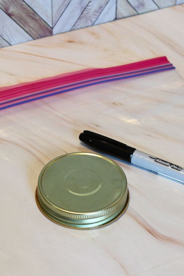 A metal jar lid, a black marker, and a set of multicolored straws are scattered on the marble surface like playful confetti from Sprinkle Squish Bags.
