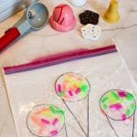 Colorful toy ice cream set with scoops, cones, and sprinkles alongside a Sprinkle Squish Bag adorned with drawn cones and vibrant sprinkles.