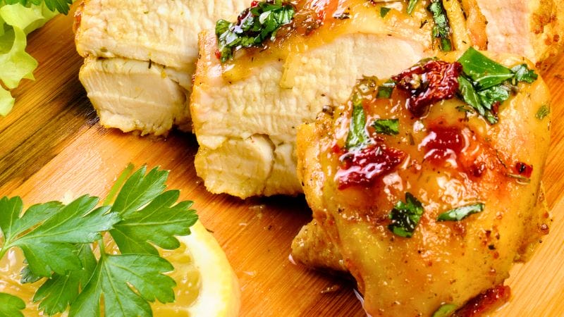 Sliced roasted chicken with herbs served on a wooden board, garnished with parsley, a lemon wedge