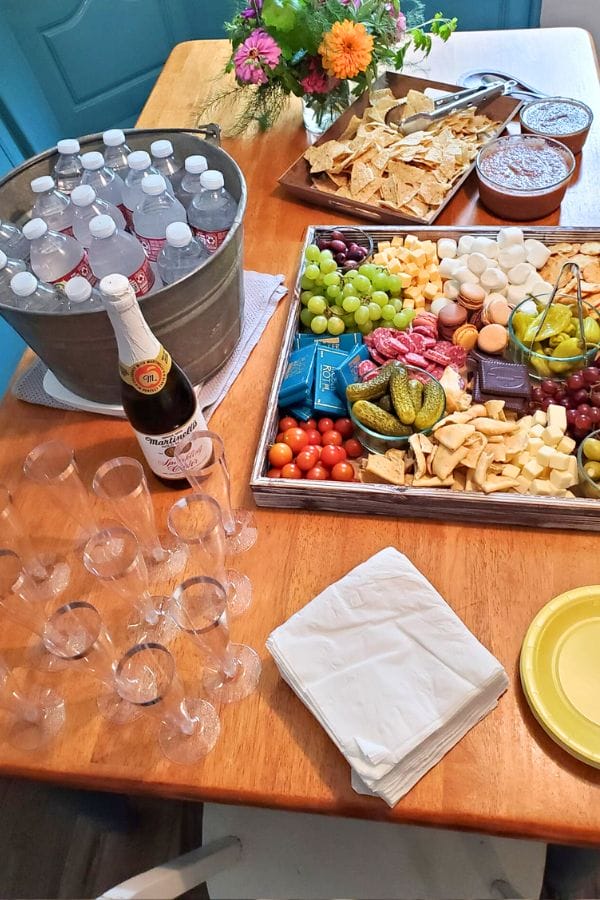 Amidst the art celebration for kids, a table brims with a vibrant food platter, crunchy chips, zesty salsa, and a refreshing bucket of bottled water. Nearby, plastic cups await the pop of sparkling juice, adding effervescent joy to this creative festivity.