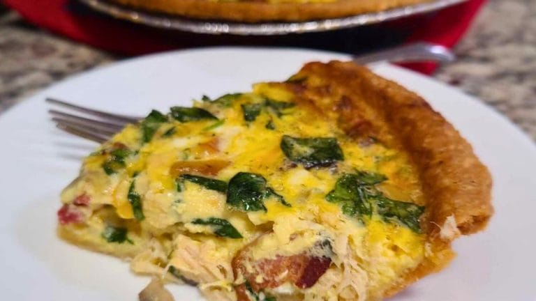 A slice of tuna, bacon, and mushroom quiche on a white plate with a fork, set invitingly on a countertop.