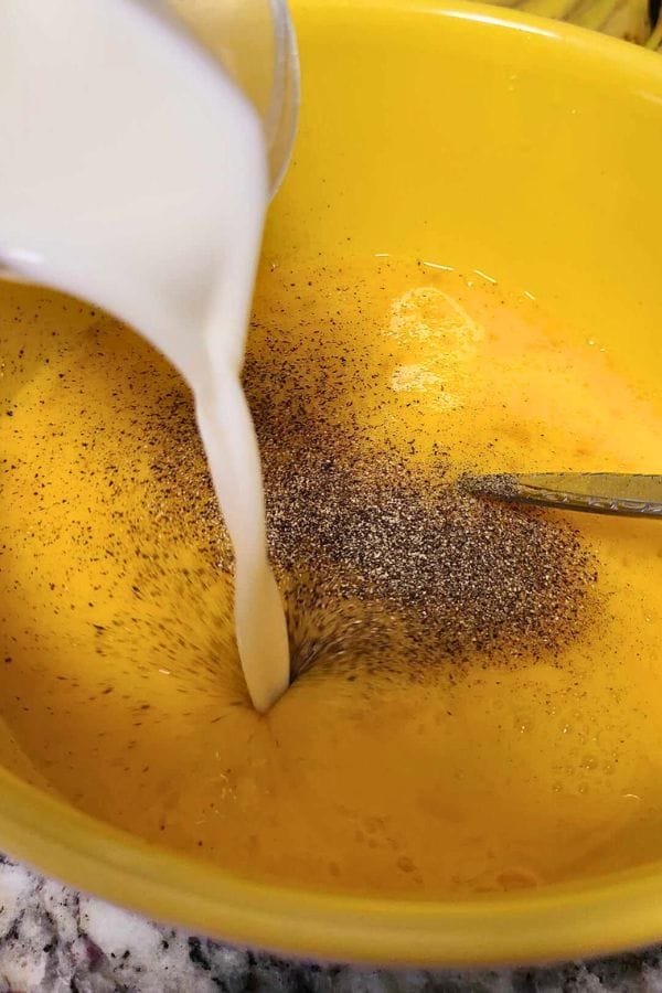 Milk cascades into a yellow bowl filled with beaten eggs and black pepper, ready to become the base for delicious Broccoli Cheese Egg Cups. A fork rests nearby, poised to mix this savory blend.