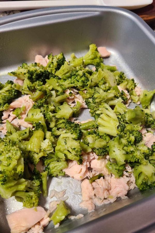 A delightful mix of chopped broccoli and pieces of cooked chicken in a metal pan, reminiscent of the simplicity and flavor of a crustless tuna quiche.
