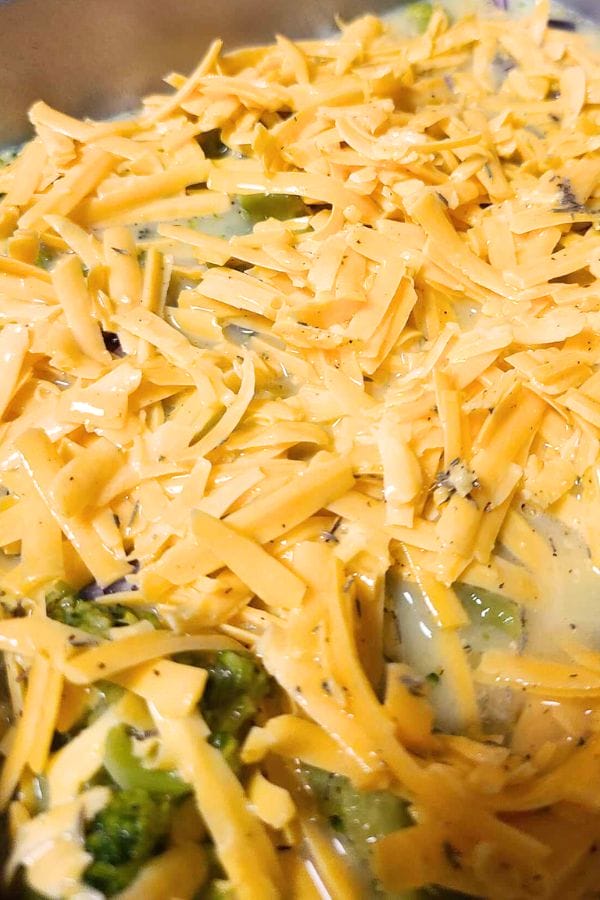 Close-up of a crustless tuna quiche featuring shredded cheddar cheese layered over broccoli pieces, all enveloped in a creamy sauce.