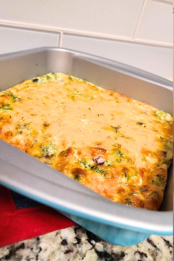 A crustless tuna quiche baked to perfection, its golden-brown top showcasing vibrant green and pink ingredients, rests invitingly on a speckled countertop.
