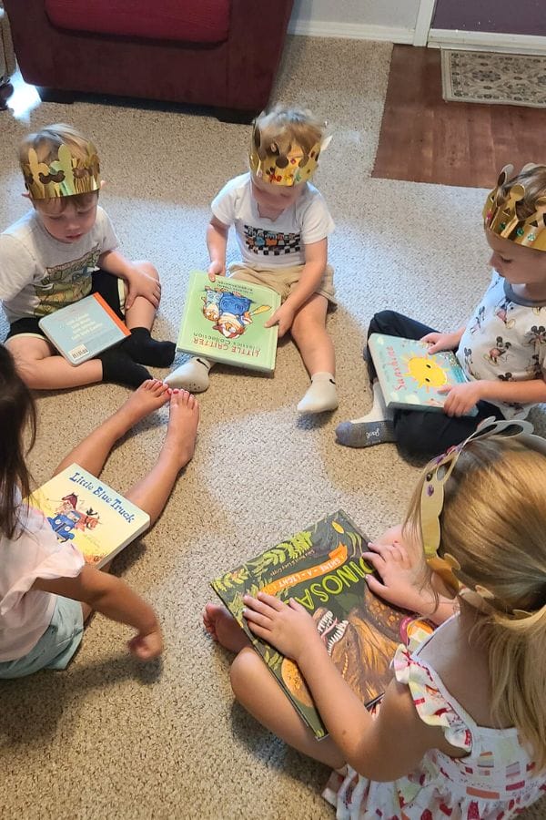 Children wearing paper crowns sit in a circle on the floor, each holding a book, as the Classic Literature Themed Tea Party unfolds.