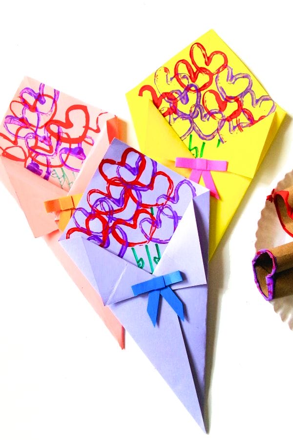 Colorful paper crafts shaped like bouquets, adorned with heart stamp designs, folded paper, scribbles, and bows, placed elegantly on a white surface.