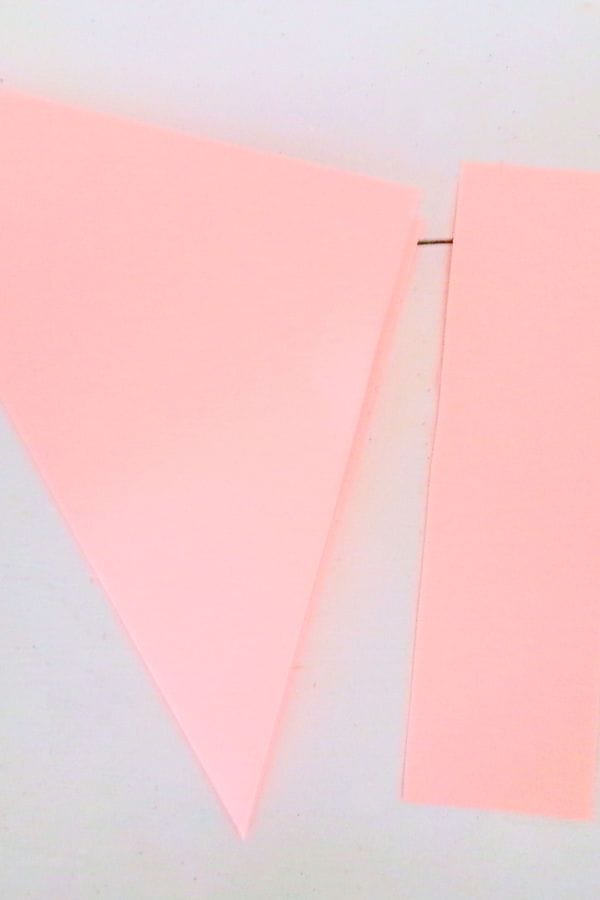 Two pink paper shapes on a white surface: one resembles a triangle, the other forms a narrow rectangle, coming together like petals in a delicate bouquet.