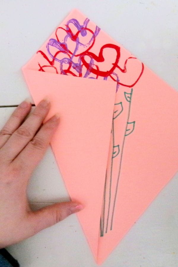 A hand holds a pink paper foldout adorned with red and purple heart shapes, resembling a delightful heart stamp bouquet.