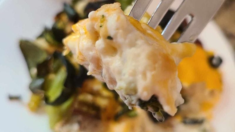 A close-up of a fork holding a cheesy cauliflower and broccoli mix over a plate, reminiscent of the creamy goodness found in jalapeno popper chicken casserole.