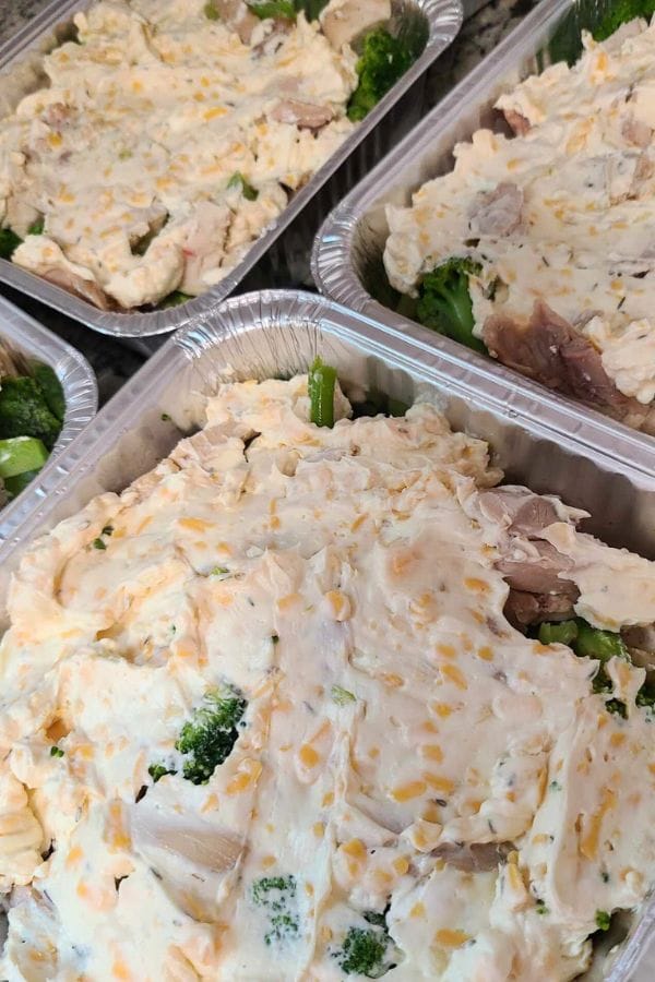 Aluminum trays filled with a Jalapeno Popper Chicken Casserole, featuring shredded chicken, broccoli, and a creamy cheese mixture.