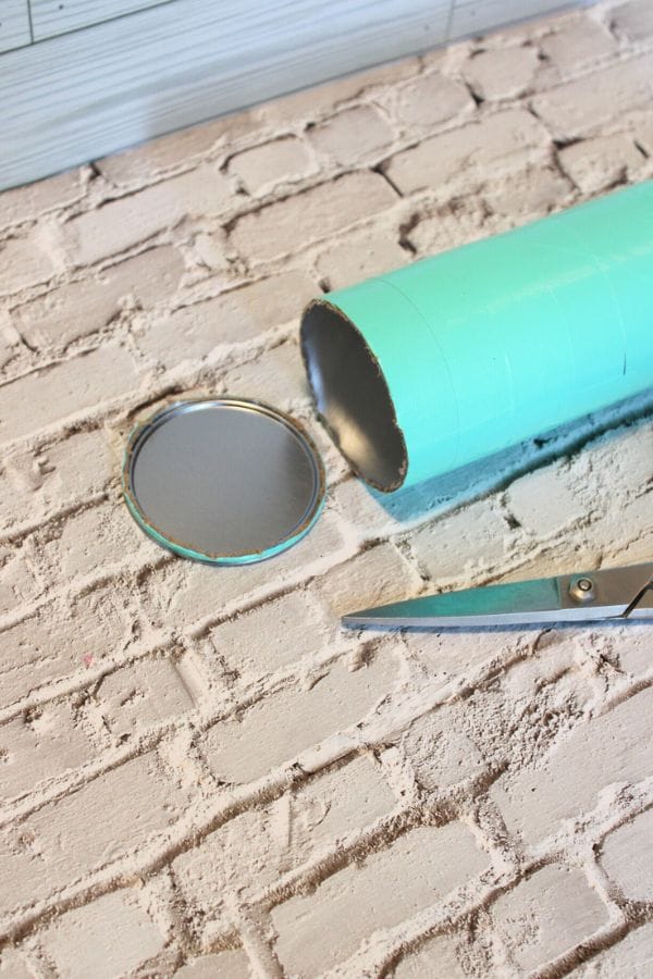 A turquoise cardboard tube rests on a textured surface, poised for a creative project. Nearby, a metal lid and scissors hint at the beginnings of DIY shadow puppets.