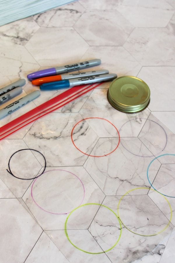 Colored markers, red straws, a jar lid, and drawn circles on marble-patterned paper come together to create a vibrant caterpillar sensory bag experience.