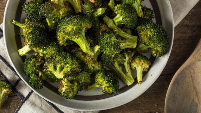 A plate of vibrant broccoli florets is artfully arranged on a wooden table, accompanied by a wooden spoon and a cheerful striped cloth, inspiring delightful broccoli recipes for kids.
