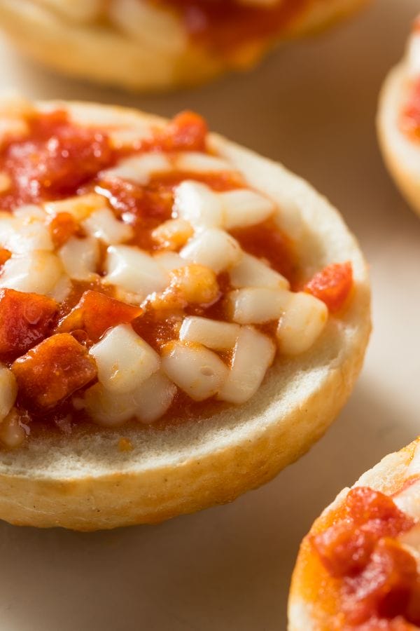 Close-up of a mini pizza bagel topped with melted cheese and diced tomatoes, perfect for meeting CN Labels for CACFP standards.