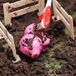 In a delightful scene of dramatic play, a pink toy pig is meticulously cleaned with a red and white toothbrush. This tiny farm animal, surrounded by dirt and enclosed in a makeshift wooden fence, brings the joy of barnyard life to every child’s imagination.