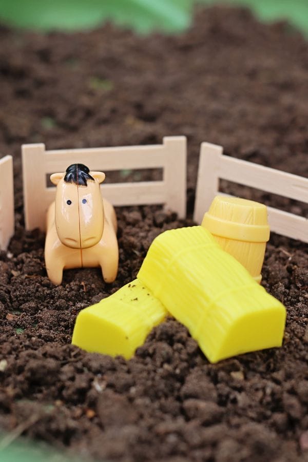 Toy horse in a fenced area with dirt, yellow haybales, and a barrel, perfect for farm animals dramatic play.