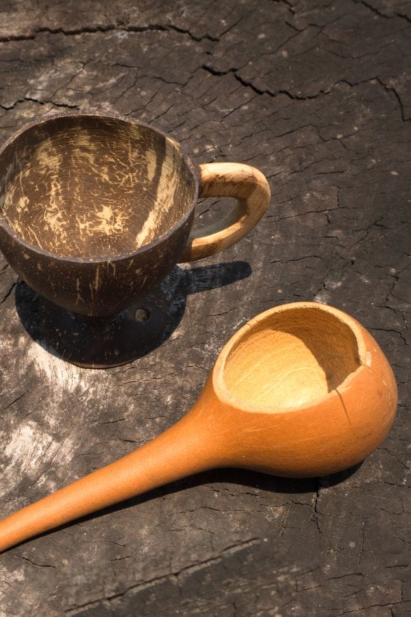 A wooden mug and a long-handled dipper rest on a textured, dark wooden surface, evoking the rustic charm of natural gourd craftsmanship.