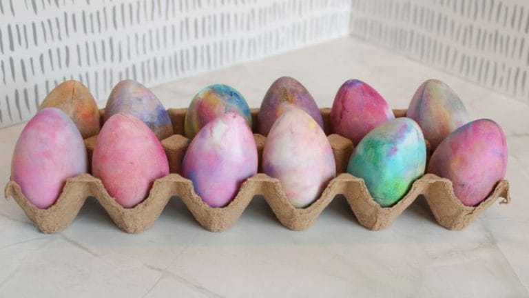 A carton of colorful, marbled eggs dyed with shaving cream rests on a patterned background.