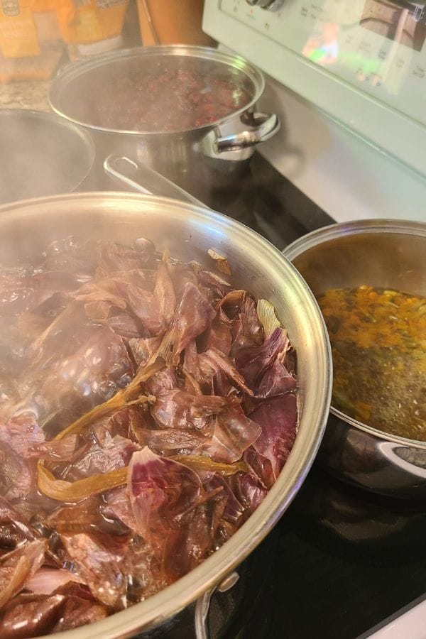 Pots on a stove with simmering ingredients, including purple leaves and herbs releasing vibrant hues akin to natural dyes, create steam above the cooking surface.